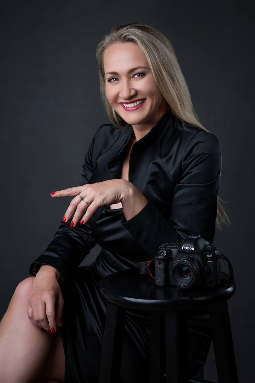 Kate Kharlamova smiling in a black satin dress beside her Canon camera in a studio portrait